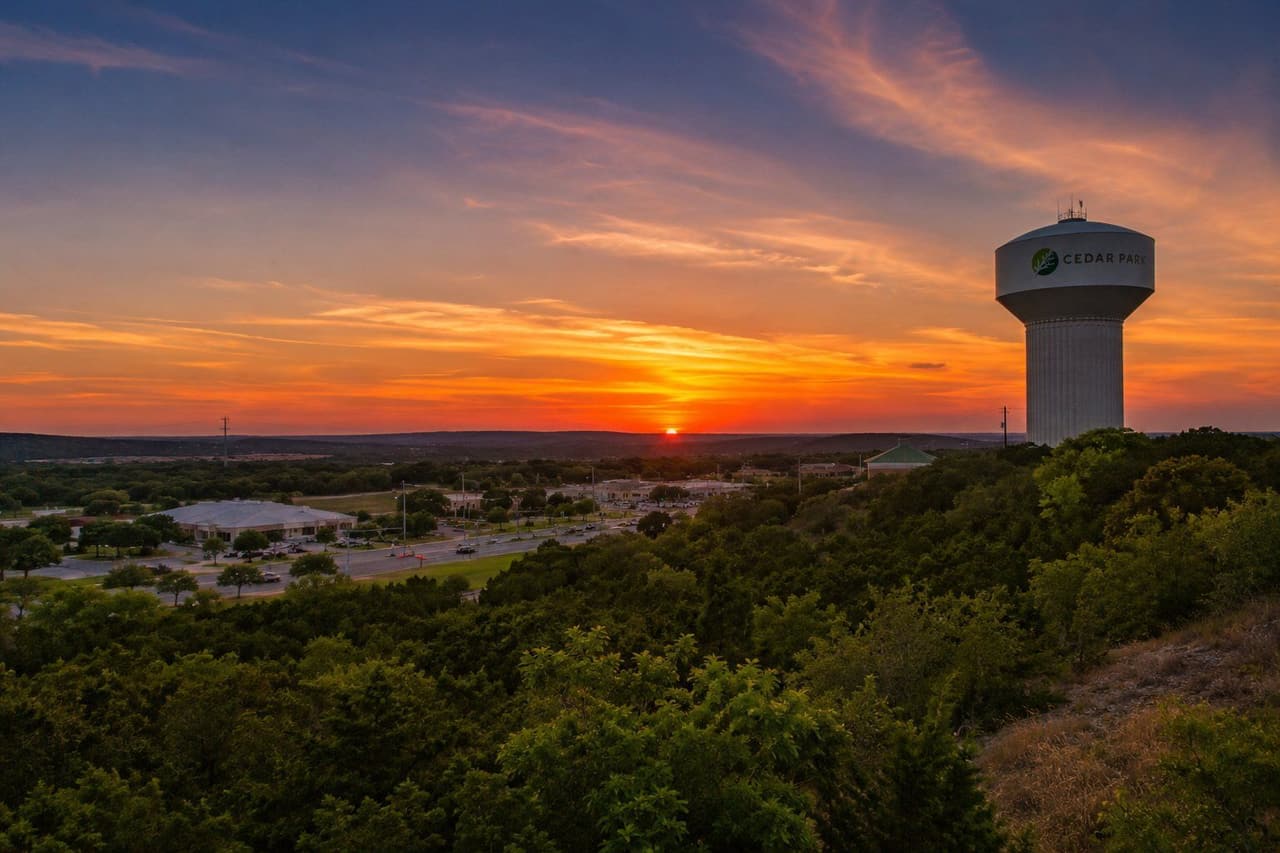 Sunset over Cedar Park, Texas — the city water tower above the hill country greenery